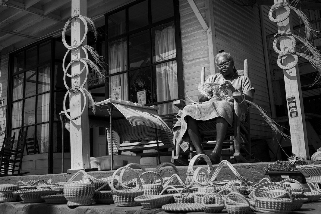 Jery Bennet Taylor naait sweetgrass manden op de veranda van Gullah Grub Restaurant. Foto met dank aan Pete Marovich